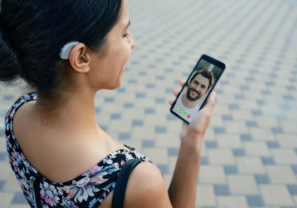 Brunette woman with a hearing aid behind the ear talking with her boyfriend on a smartphone via bluetooth connection